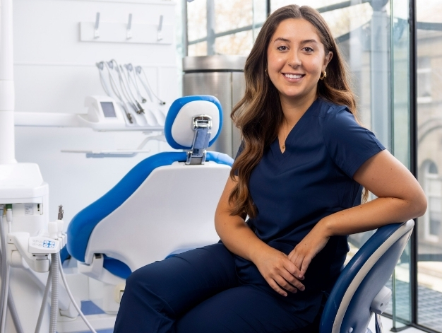 Inez Duane sitting in the dentist's chair, wearing blue dentist scrubs and smiling at the camera