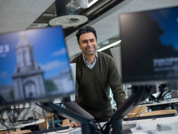 Taha Yasseri smiling at the camera from between two computer monitors